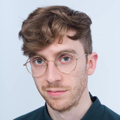 Man with short curly hair and glasses looking straight at camera
