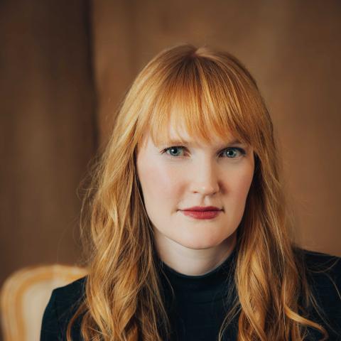 Woman with long red hair over shoulders and black t-shirt smiling slightly at camera