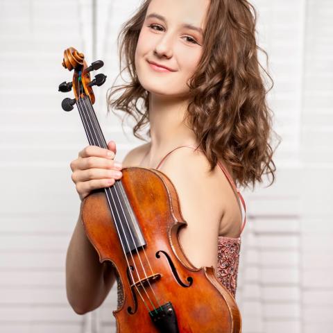 Anna Stube is holding a violin and looking towards the camera smiling