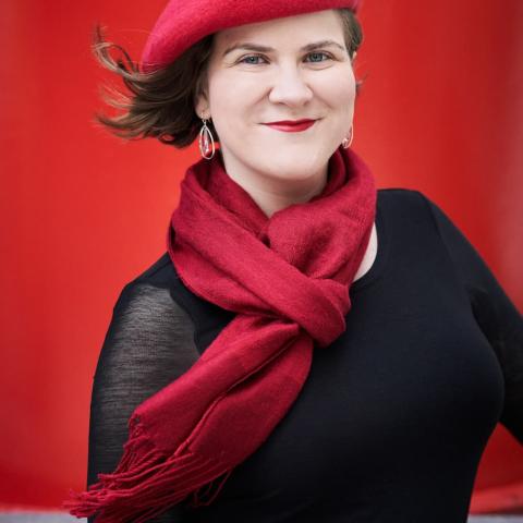 Ema Nikolovska is wearing a black top, red scarf and red beret, and smiling at the camera