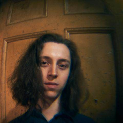 Man with long shoulder length hair standing against door looking at camera