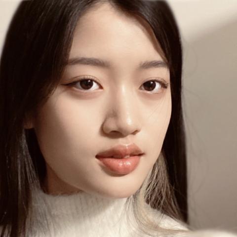 Close up headshot of a woman with brown hair and wearing a white sweater looking directly at the camera