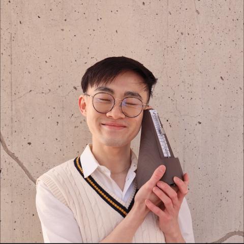 Man holding metronome against face while smiling with eyes closed at the camera