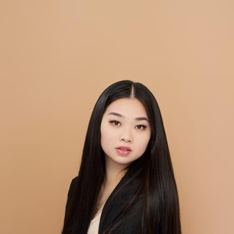 Woman sitting in suit jacket in front of orangish background looking directly at the camera