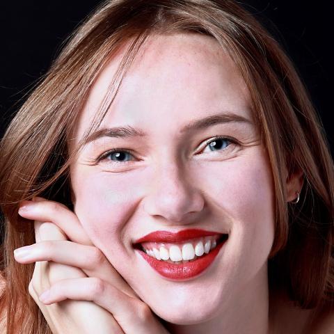 Close up shot of woman smiling broadly at camera with face leaning against clasped hands