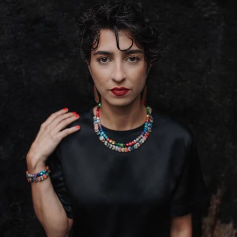 Person in black top and colourful necklace looking directly at the camera