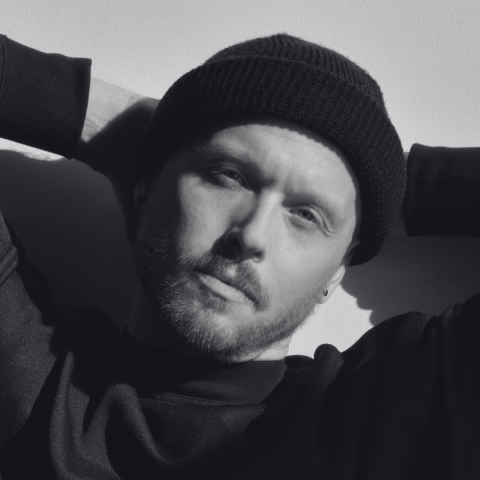 Black and white photo of man with arms behind head and wearing a toque