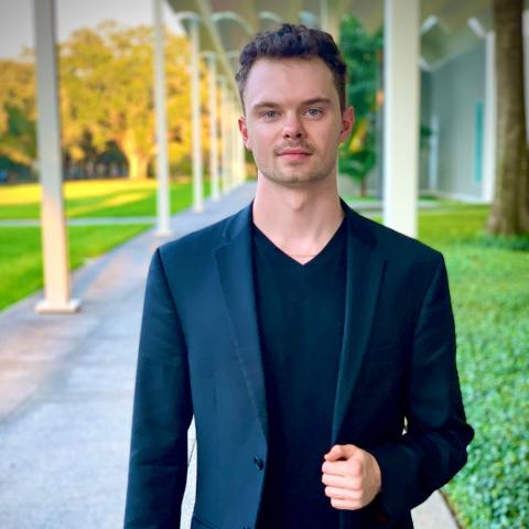 Man outside on a walkway in a dark suit staring directly at camera