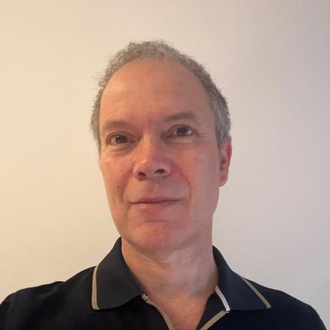 Man smiling directly at camera wearing close cropped hair and a black polo shirt