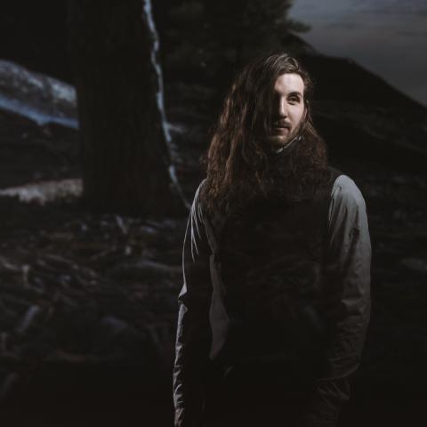 Man standing in front of fence in dark photo where only face is light
