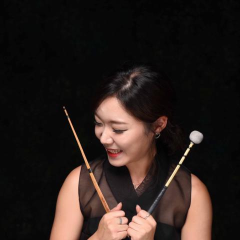 Person smiling with drum sticks looking off to the side