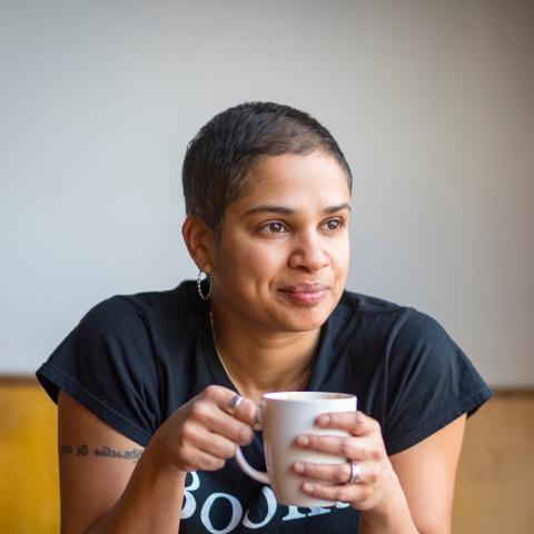 Photo of program faculty, Tanya Boteju, relaxed and smiling, leaning forward with coffee mug held in both hands