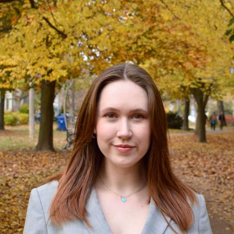 Long, red haired woman smiling directly at the camera with colourful fall leaves behind her