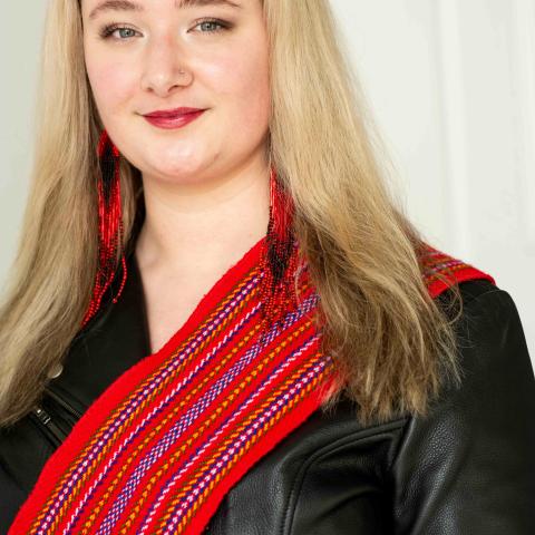 A long haired woman wearing a Metis sash and a leather jacket