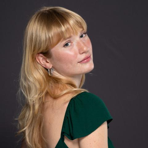 Woman wiht long blond hair looks over her right shoulder to smile into the camera wearing a green formal dress