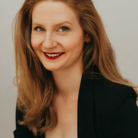 Woman with long light brown hair smiling at the camera in a dark jacket