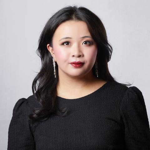 Woman with long black hair slightly smiling and staring directly at the camera in a black dress