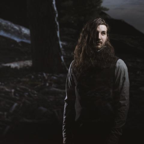 Jonathan stands and looks to the right. The photo is dark and very intriguing. 