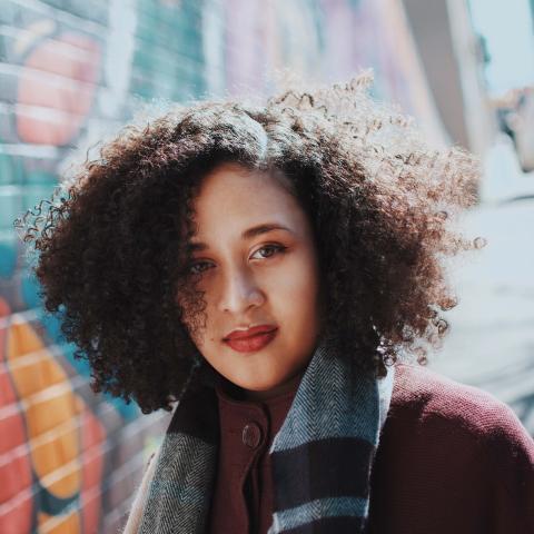 Alyssa looks at the camera with a scarf in front of a brick wall. 