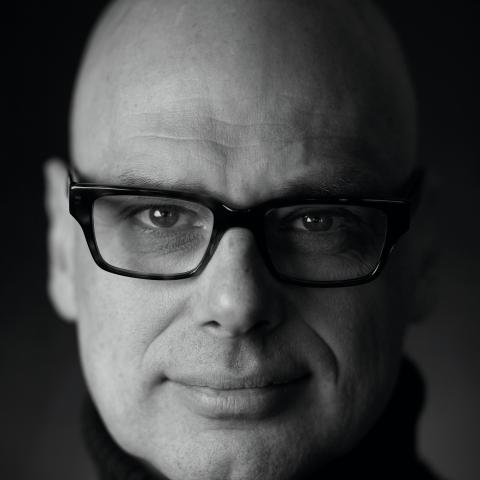 Multi-media designer, Hugh Conacher, wears glasses in a black and white photo