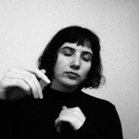 Black and white photo of Marie with their eyes closed, wearing a black shirt in a bit a movement shot. 