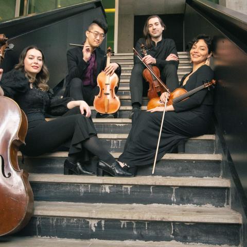 The Ximenez Quartet sits on stairs holding their instruments. They smile at the camera. 