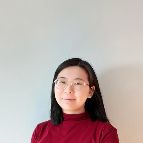Futian wears a red shirt and stands in front a white wall. 