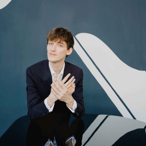 Sean Morgan-Rooney sitting behind a piano with reflection on piano surface
