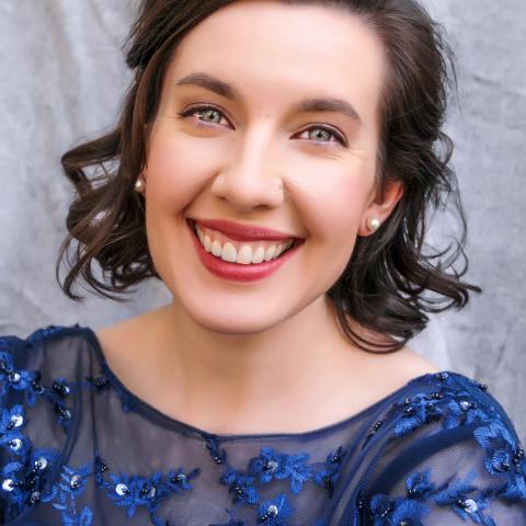 Woman with shoulder length curly hair smiling directly at the camera wearing a blue formal dress