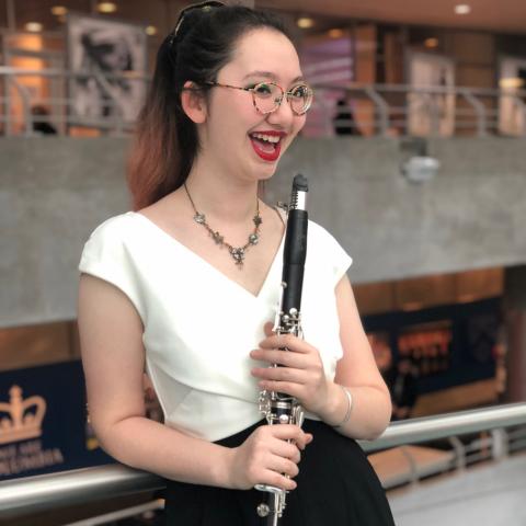 Woman leaning against a railing holding a clarinet with both hands in front of their chest
