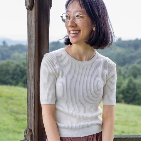 Person with shoulder length hair and white shirt looking into the distance smiling
