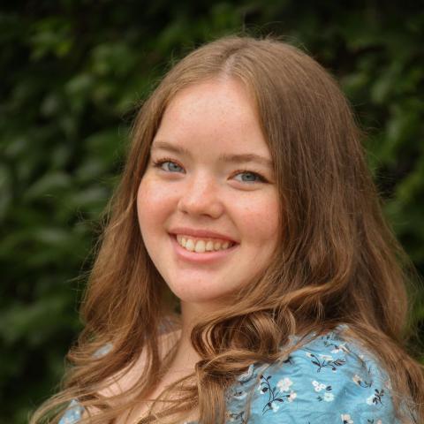 Woman with blue floral dress smiling directly at camera with light brown hair falling over shoulders