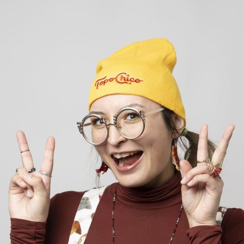 Woman with large smile and yellow toque giving two peace signs to the camera