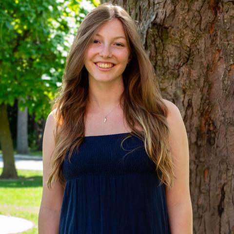 Woman in blue dress with long brown hair smiling at the camera