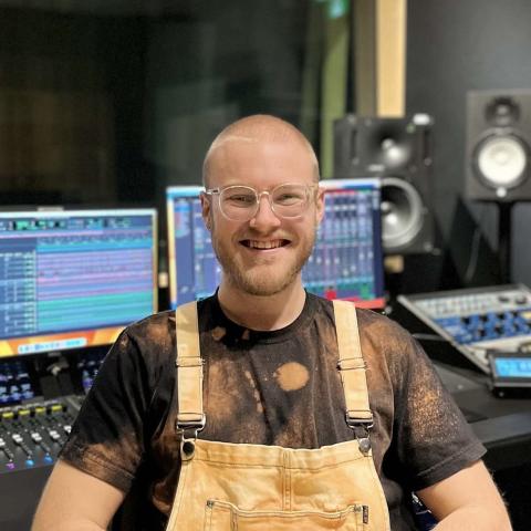 Man smiling broadly at camera in front of audio equipment 