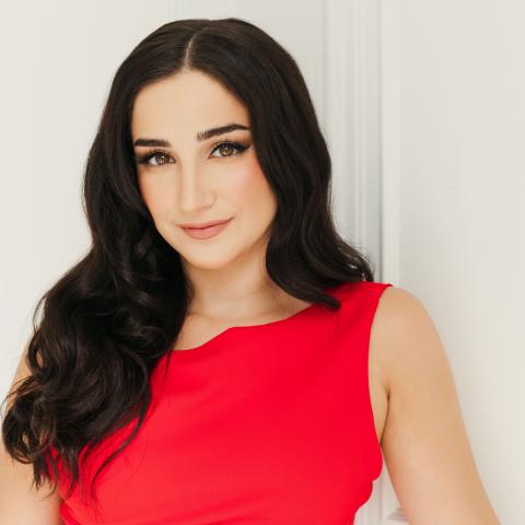 Woman with long black hair covering shoulders smiling lightly at camera in bright red dress
