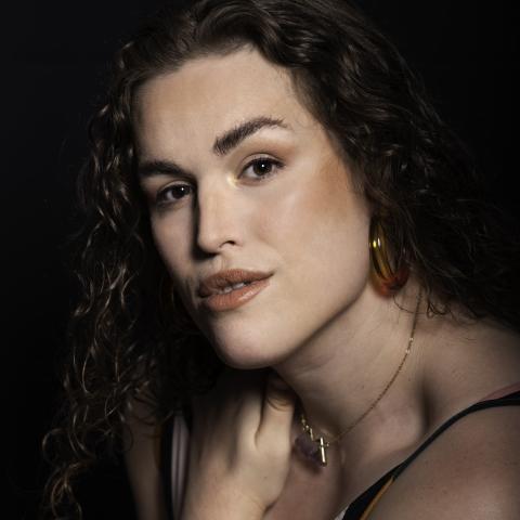 Woman with hand across chest and holding shoulder looking directly at camera