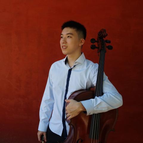 Man holding cello and standing against red wall