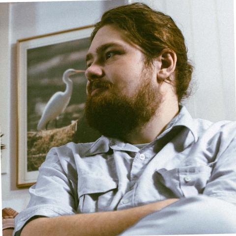 Man with hair pulled back and a beard looking off to the left off camera with arms crossed