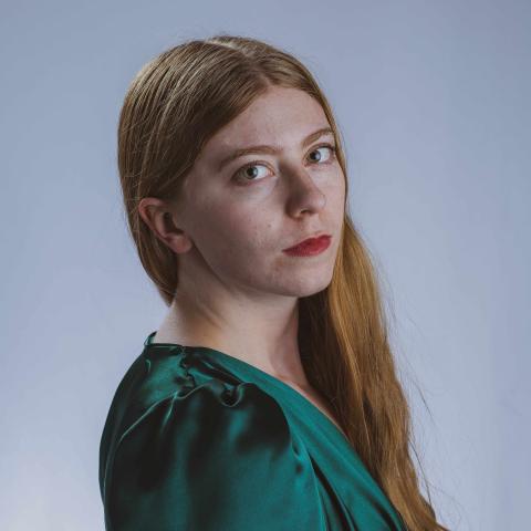 Woman with long red hair cascading over her shoulder, looking to the side directly at camera in bright green dress