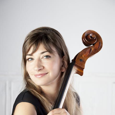 Cellist smiling at the camera with arms wrapped around cello