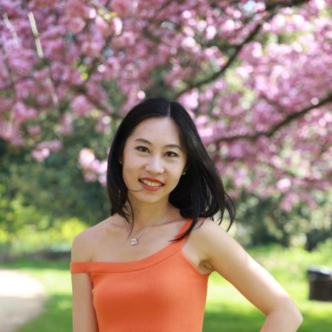 Woman standing confidently in bright orange dress in front of cherry blossoms