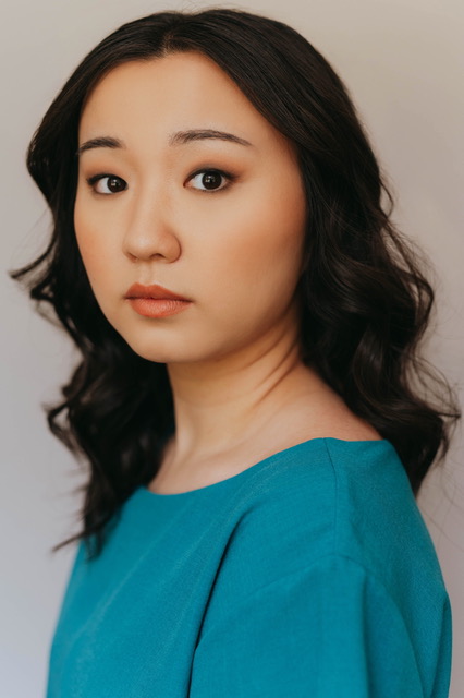 Woman with black wavy hair looking to the side at the camera in a teal blouse