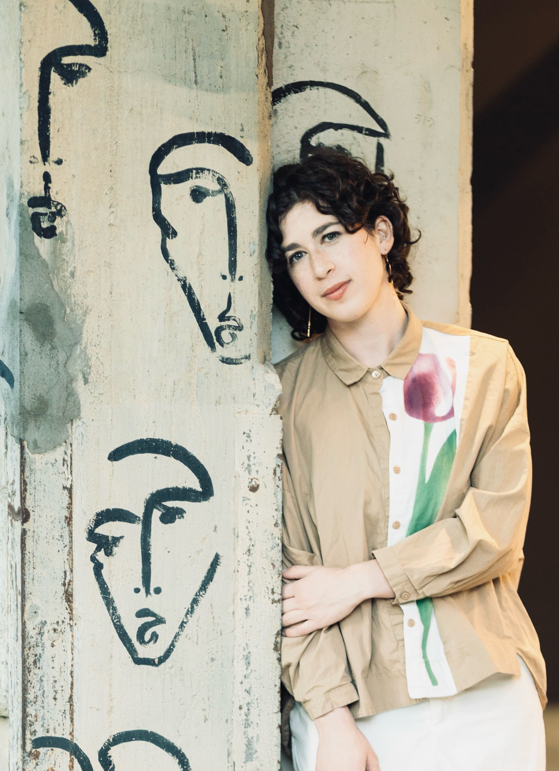 Woman leaning against art wall smiling lightly at camera