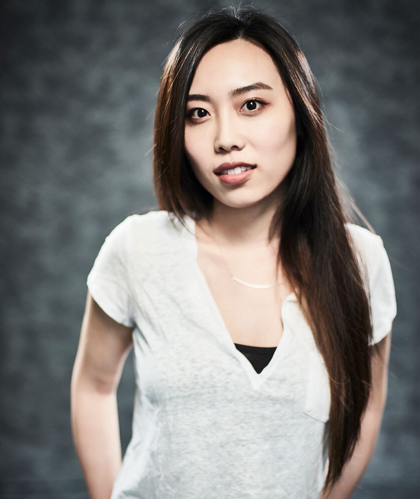 Woman in white t-shirt with hands behind back in pant pockets smiling at the camera